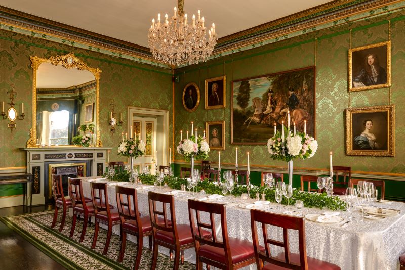 Elegant room with framed classic art, long set table and centerpieces of flowers and greenery