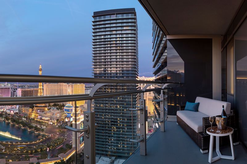 Guestroom terrace with glass railing overlooking Las Vegas skyline and Fountain at night