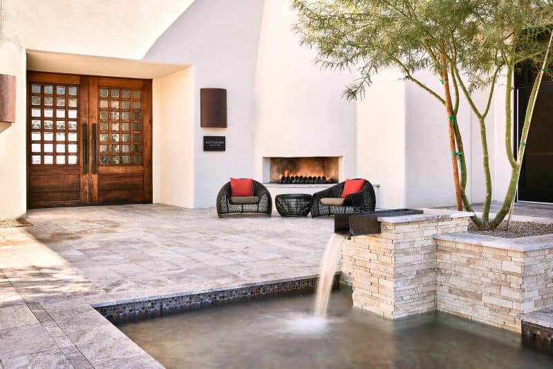 Exterior courtyard with water feature and black wicker chairs by fireplace and large wooden doors