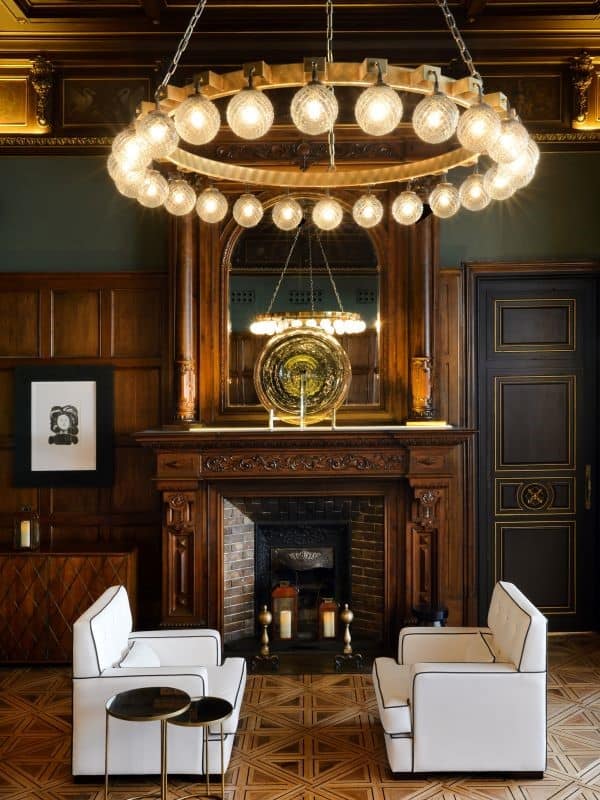 Two modern white sofas in front of handsome carved wood fireplace & a circular chandelier