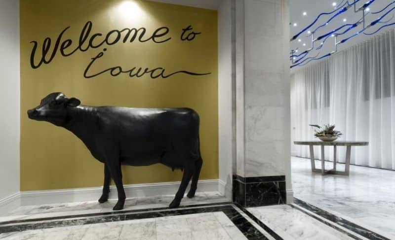 Cow statue in front of gold colored wall with the words “Welcome to iowa”