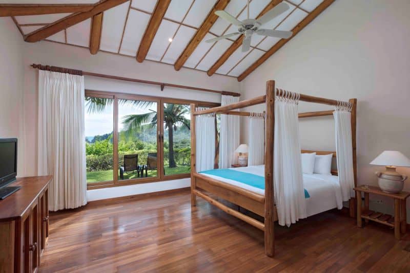 Bedroom with canopy bed, high ceilings and view of palm trees and greenery through window