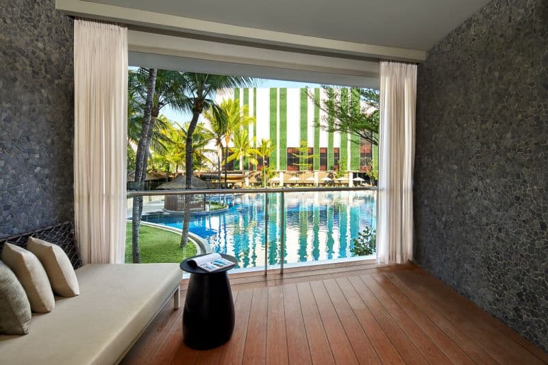 Guestroom sitting area with view of pool and vertical garden through floor-to-ceiling windows