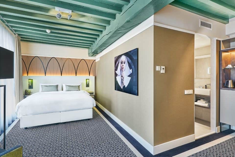 Guest room with king bed, pale green beamed ceiling, and LED TV