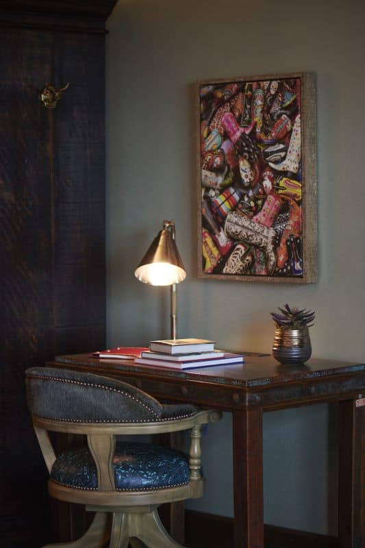 Desk with stylish blue chair, books, lamp, and framed art with cowboy boots above