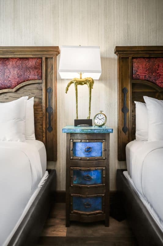 Nightstand with blue drawers between two beds with white linens and red wooden headboards
