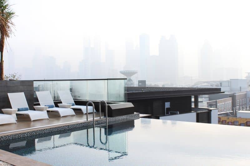 Rooftop infinity pool with lounge chairs overlooking misty city skyline